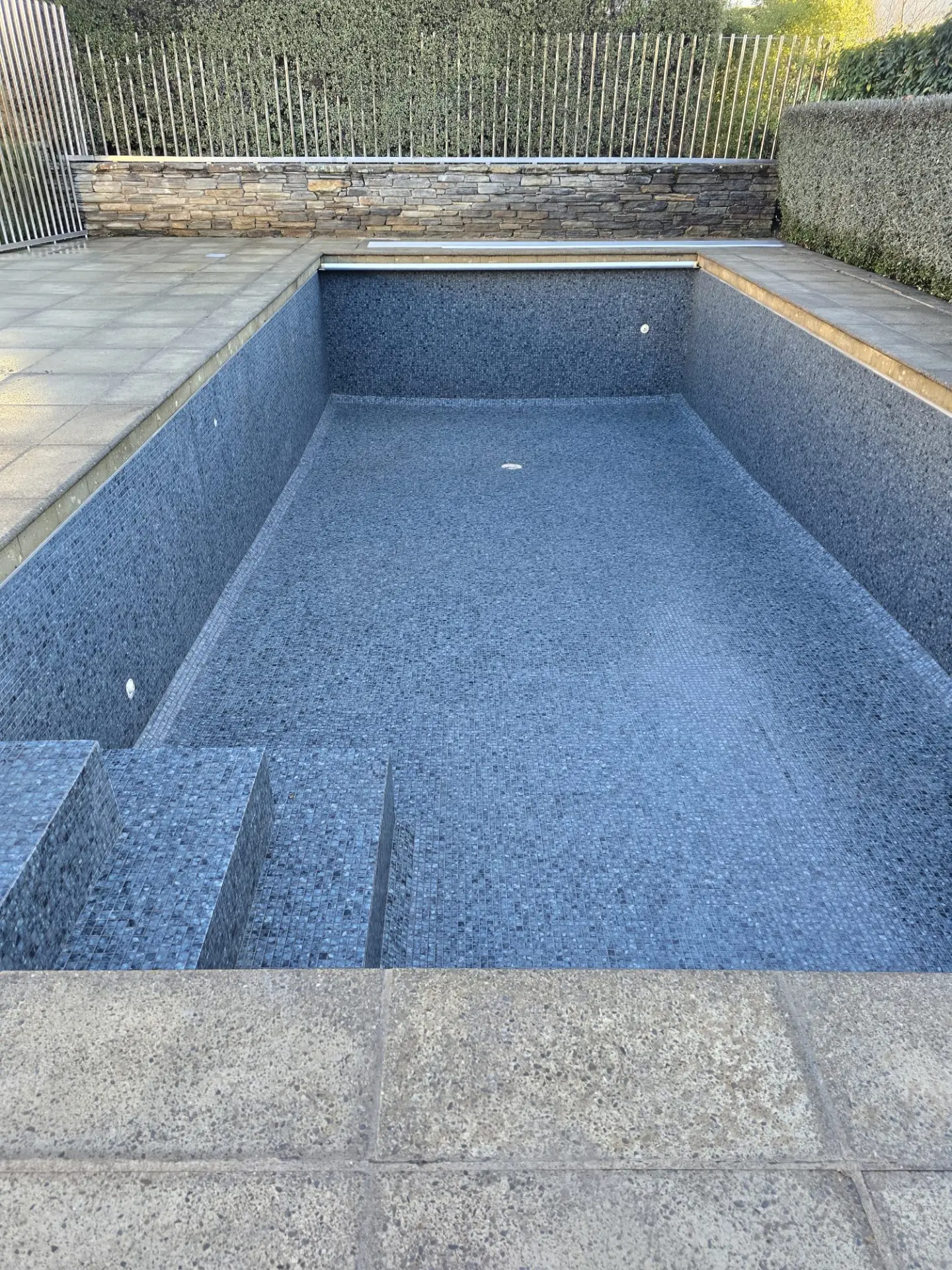 Pool fully retiled in dark grey mosaic with stone coping and steps