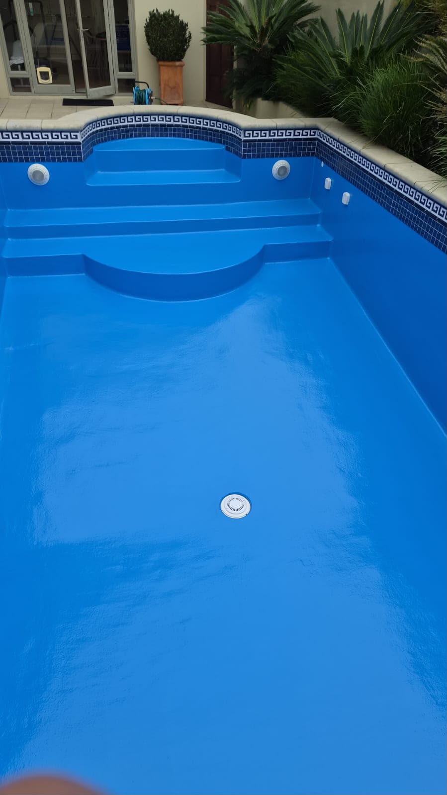 Drained pool freshly coated in mid blue epoxy with original waterline feature tiles