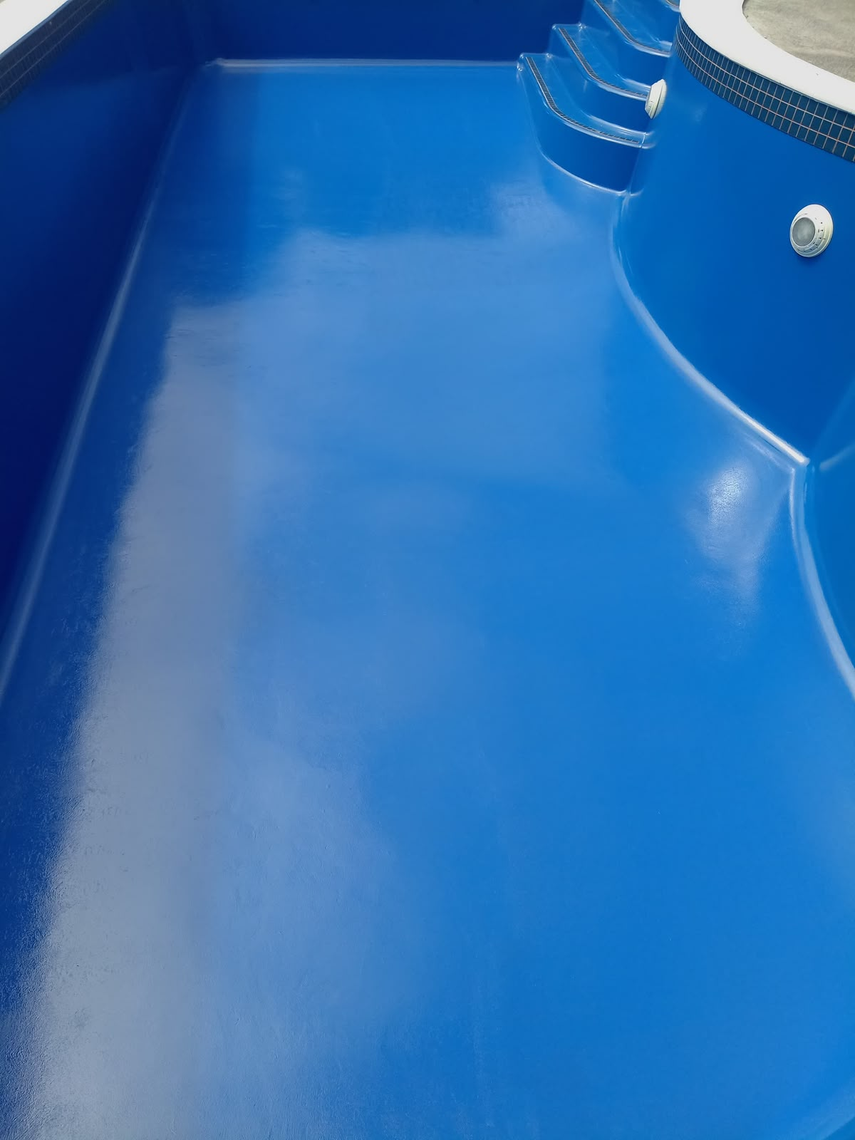 Pool interior freshly coated in bright blue epoxy with steps and light fitting